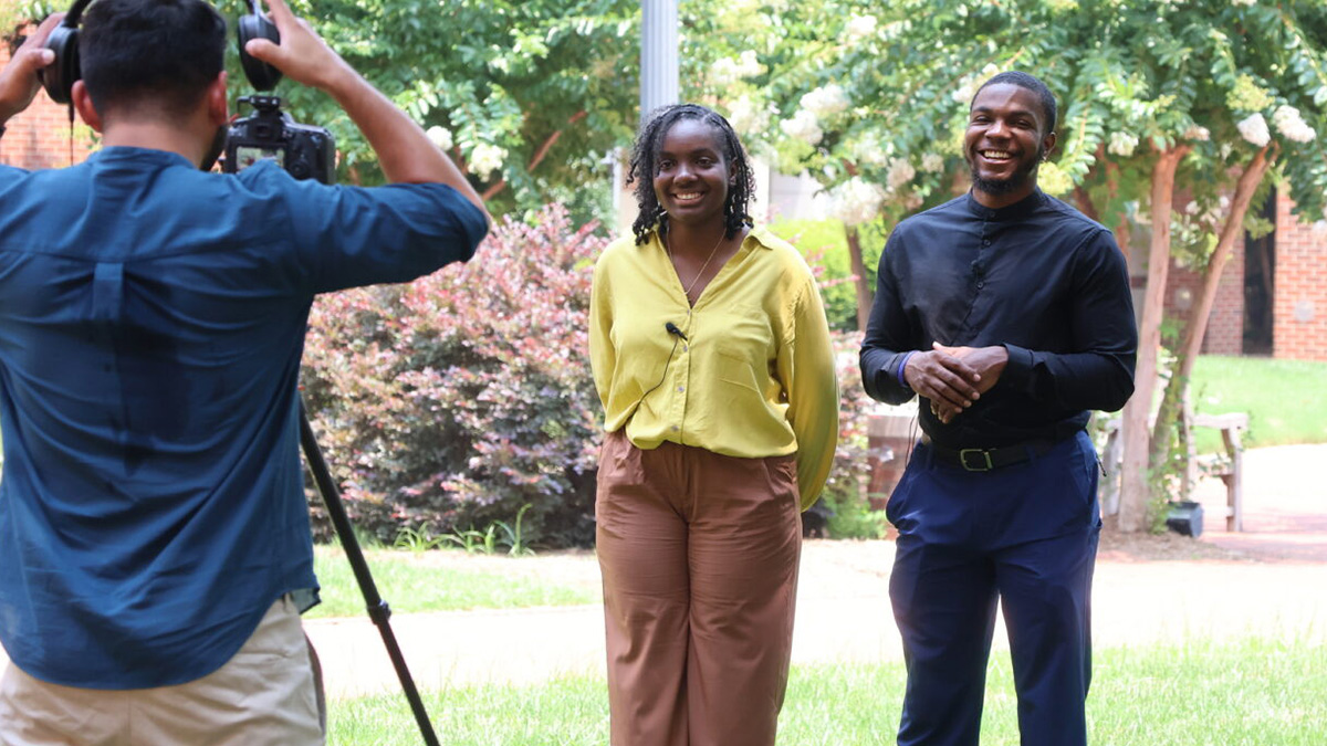 Ilianamaria and Elijah Brown film CCAC promos with Iliana wearing a yellow shirt and khaki pants and Elijah wearing an all-black suit.