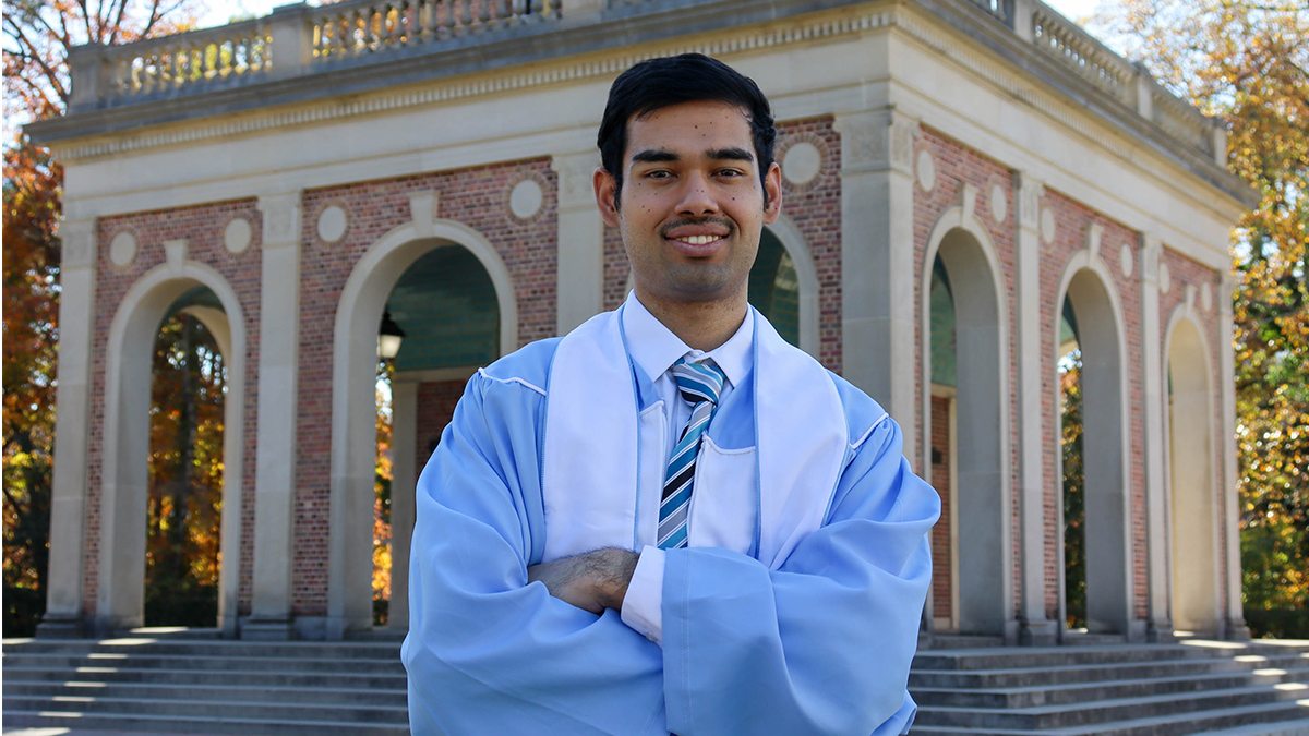 Pramit posing in front of bell tower with Carolina Blue ceremonial robes.