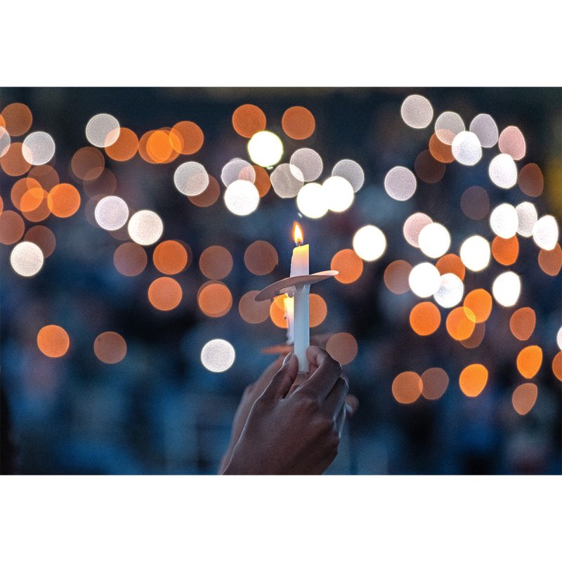 A hand holding a lit candle at a vigil.