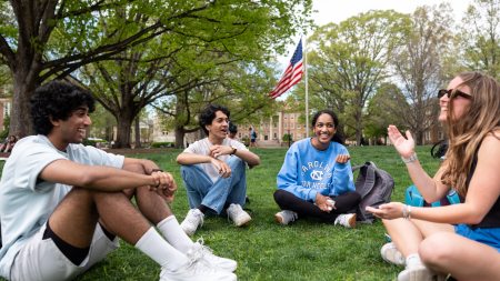 Four students talking and sitting on the lawn of McCorkle Place on the campus of UNC-Chapel Hill