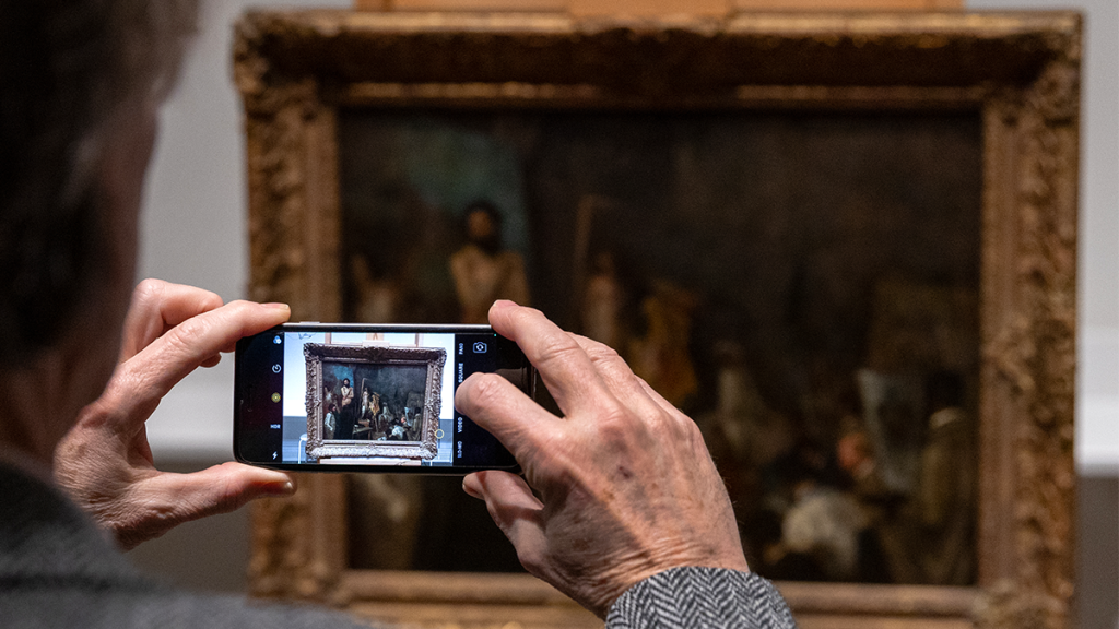 Visitor takes photo of "The Studio of Thomas Couture" on their phone. 