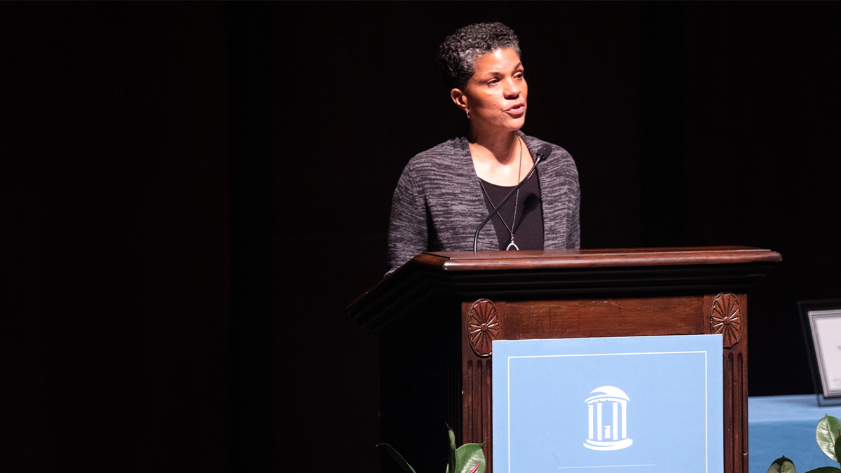 A woman, Michelle Alexander, speaking from a podium on a stage at a lecture.