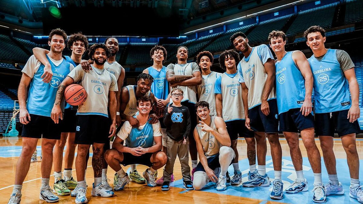 The UNC men's basketball team taking a team photo on the court of the Dean E. Smith Center with a 9-year-old boy, Colburn Dean.