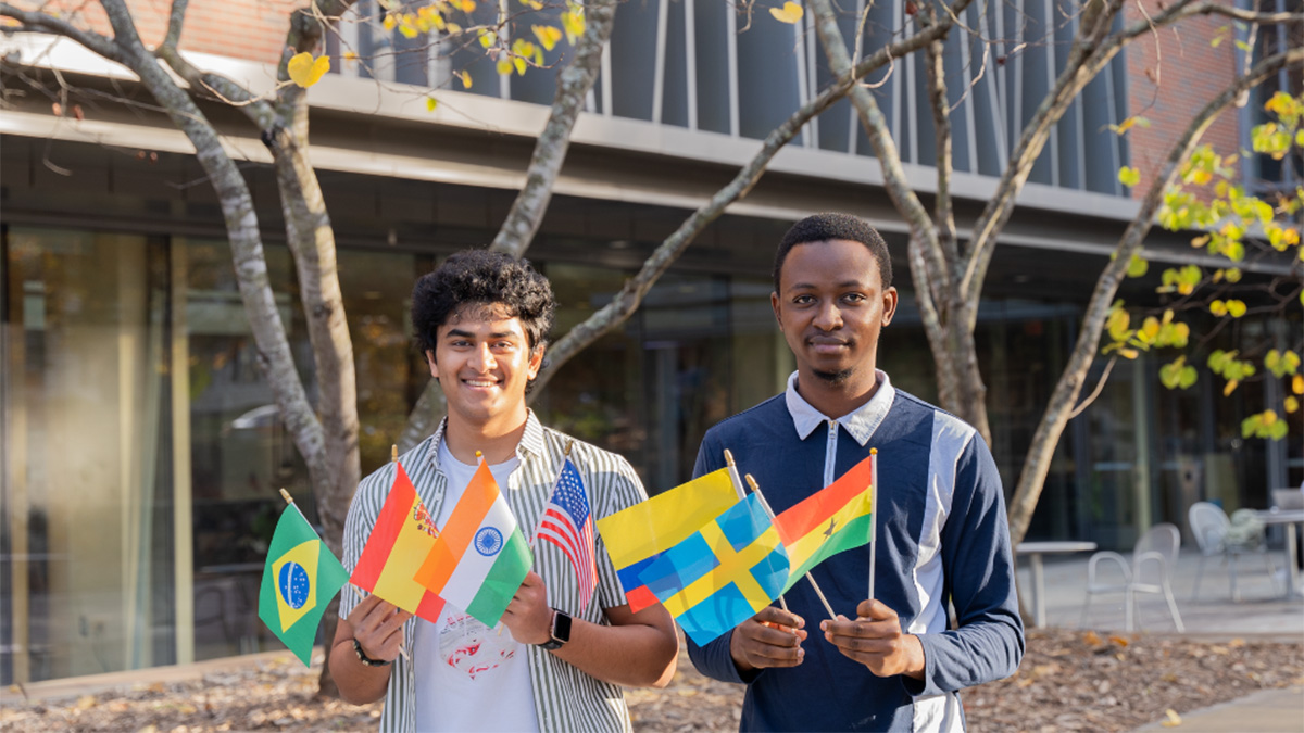 Two students, Satvik Chethan and Jim Appiah, holding several small flags of different nations.