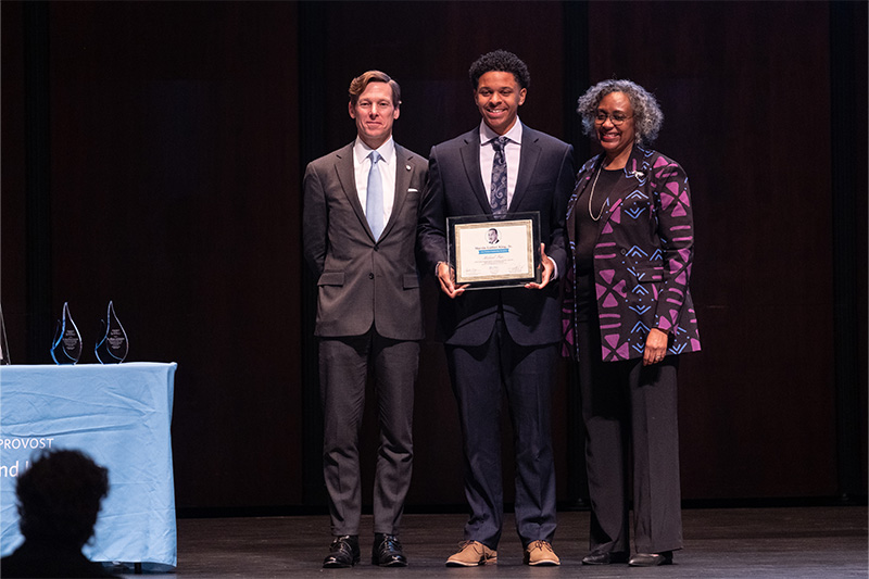 A student, Michael Fair, taking a group photo with two other people on stage, Lee H. Roberts and Leah Cox, after winning an award.