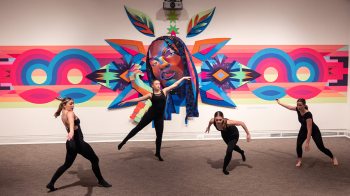 Dancers dancing in front of a large tapestry art display.