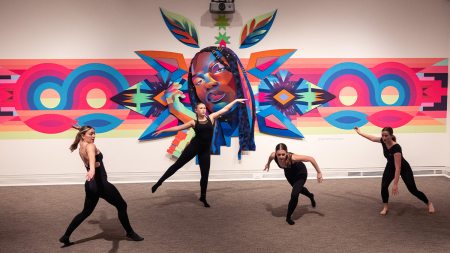 Dancers dancing in front of a large tapestry art display.