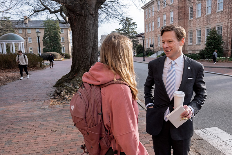 A student speaking with Interim Chancellor Lee H. Roberts on a brick pathway on the campus of UNC-Chapel Hill.