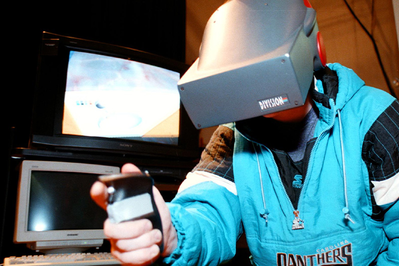 A student using a virtiual reality headset and handheld controller at a late 1990s tech fair at UNC-Chapel Hill.