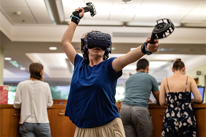 A student using a VR headset and handheld devices in the Undergraduate Library on the campus of UNC-Chapel Hill.