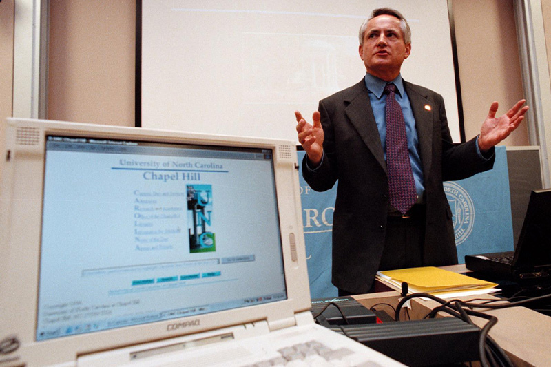 a man speaking next to a 1990s era computer.