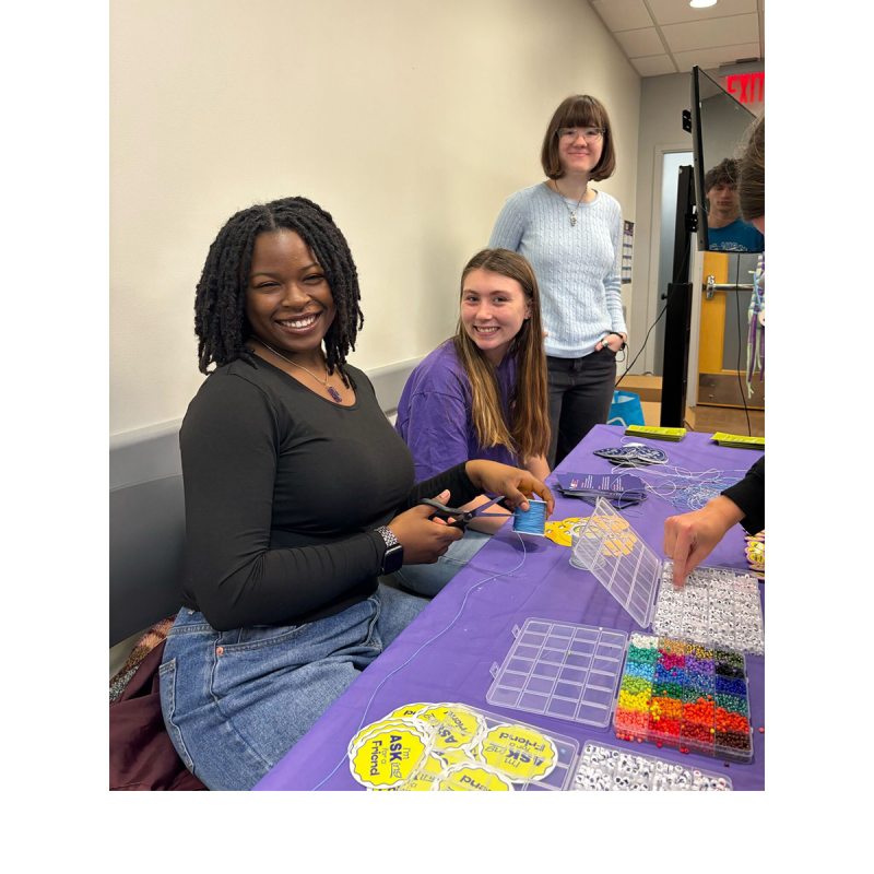 Three students sitting at a table and posing for a photo during a craft activity.