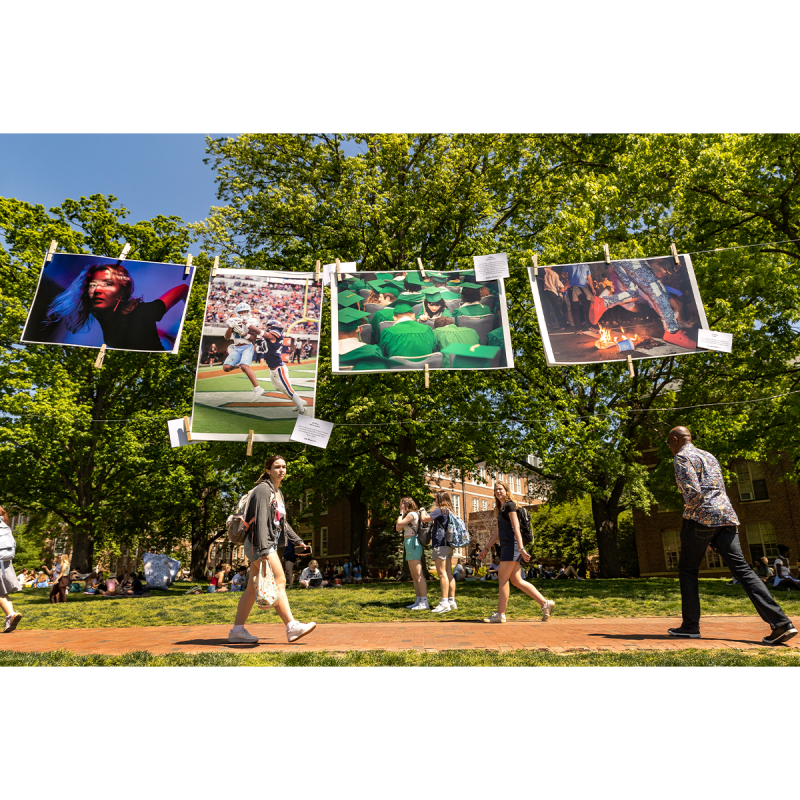 Students walking on brick pathways on the campus of UNC-Chapel Hill with art seen hanging on a clothes line.