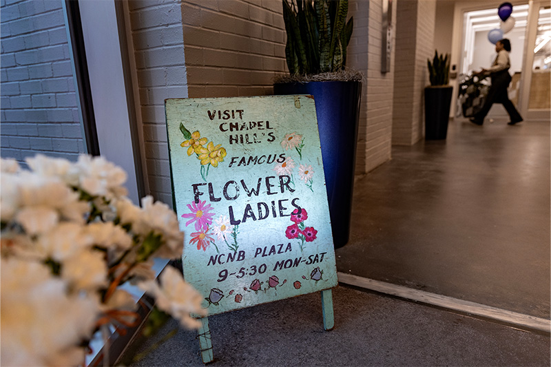 A sign reading, "Visit Chapel Hill's famous Flower Ladies. NCNB Plaza, 9-5:30 MON-SAT"