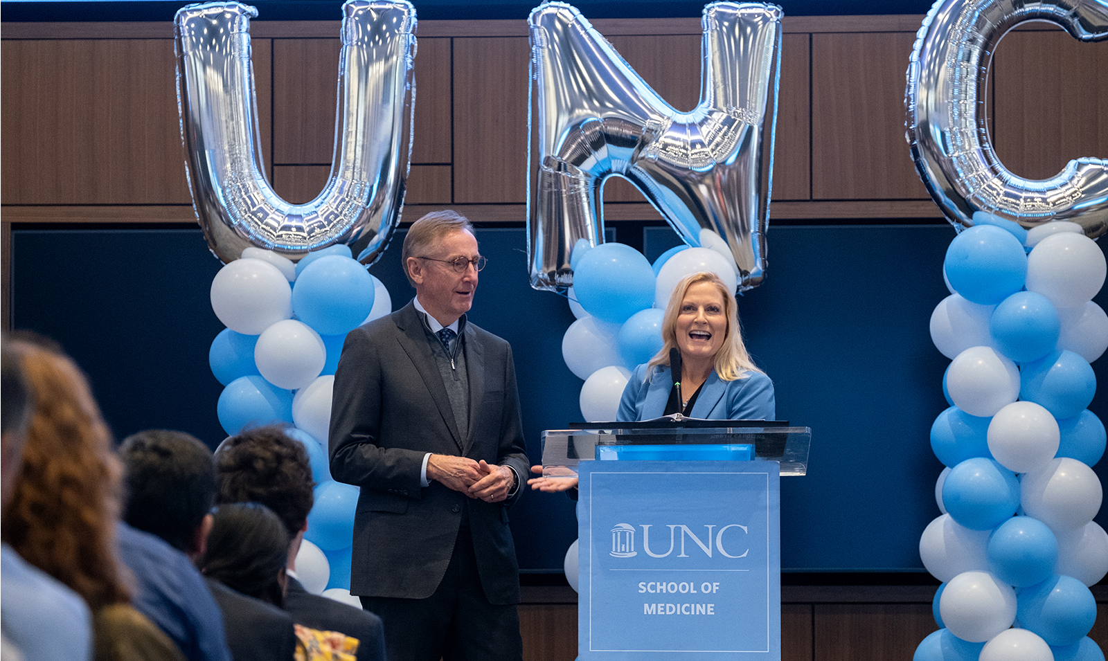 Man and woman at podium in front of UNC balloons