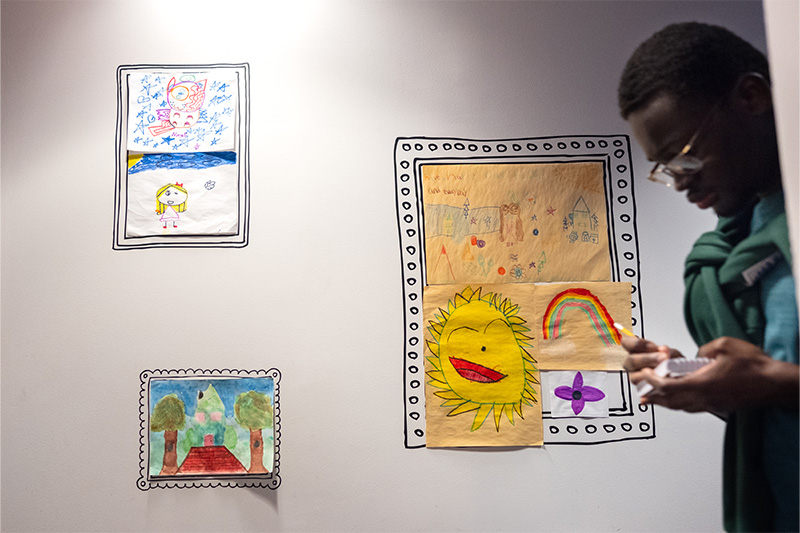 A UNC-Chapel Hill student, Twumasi Duah-Mensah, takes notes on a notepad as he walks the hallways of Pat's Place in Charlotte. Children's artwork hangs on the wall behind him.
