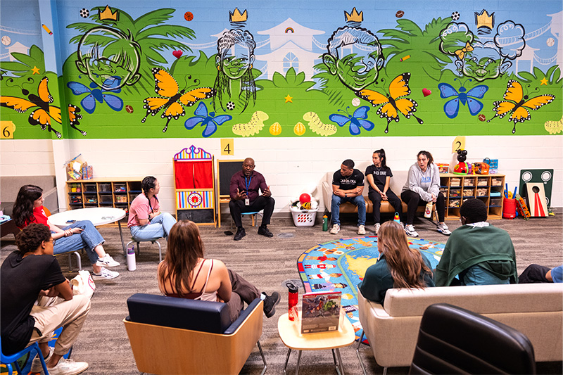 Timothy Bradley, a Mecklenburg County employee, talks with UNC-Chapel Hill students in a large open room full of toys and a large painted mural.