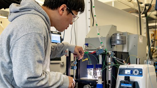 Hueynwoo Yang wearing grey sweatshirt and filling liquid vials with machinery.