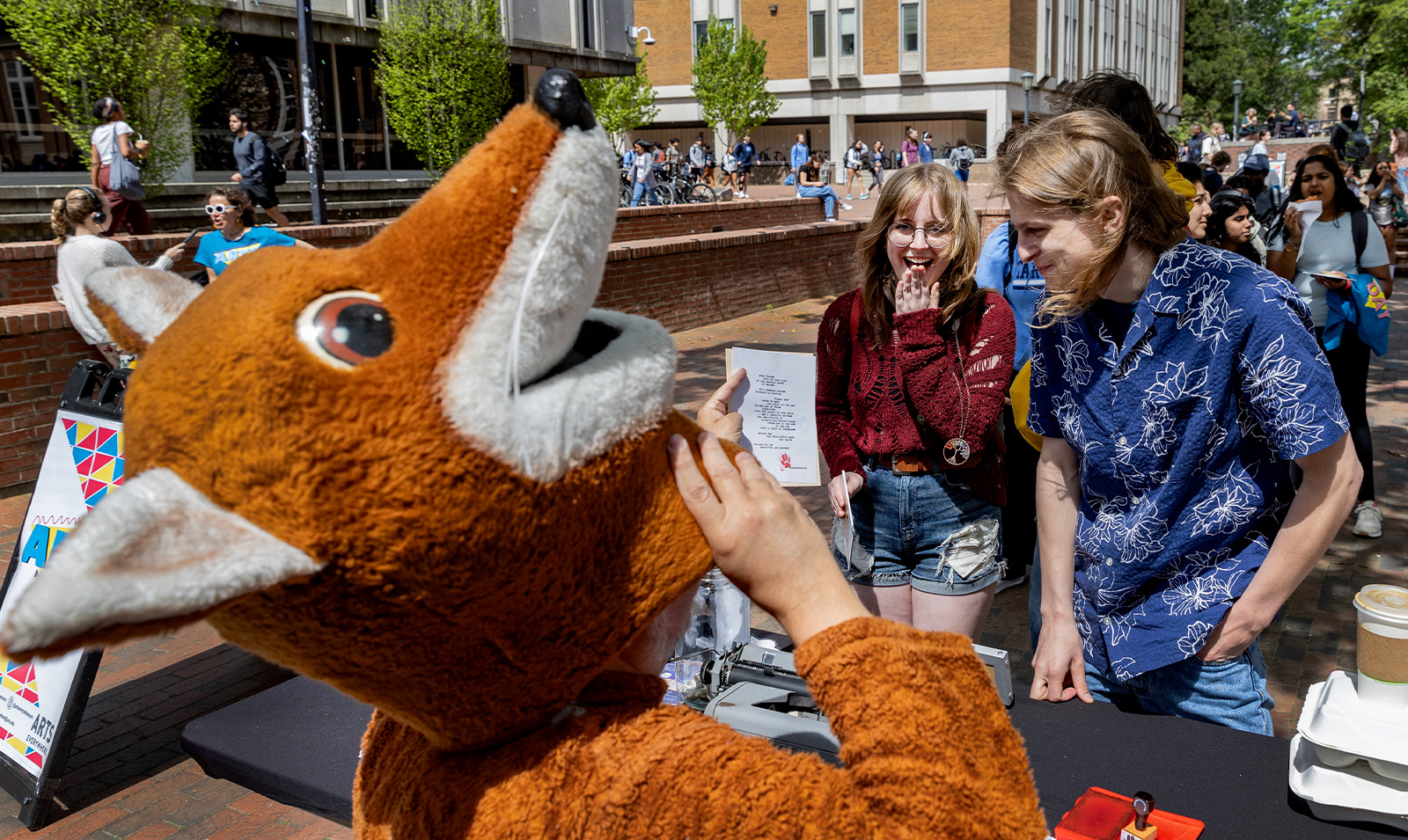 A man in a fox costume, known as the poetry fox, reading a poem he wrote to people standing in line.