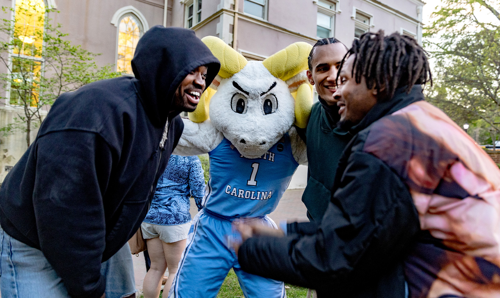 The UNC-Chapel Hill ram mascot, Rameses, huddled with three students.