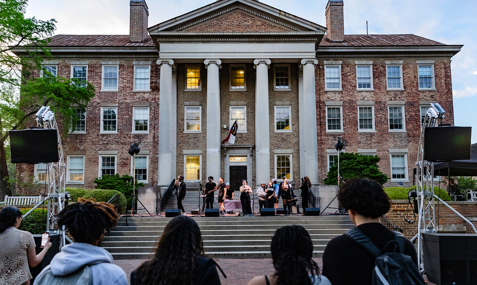 A band performing on the steps of South Building. In the foreground are students watching.