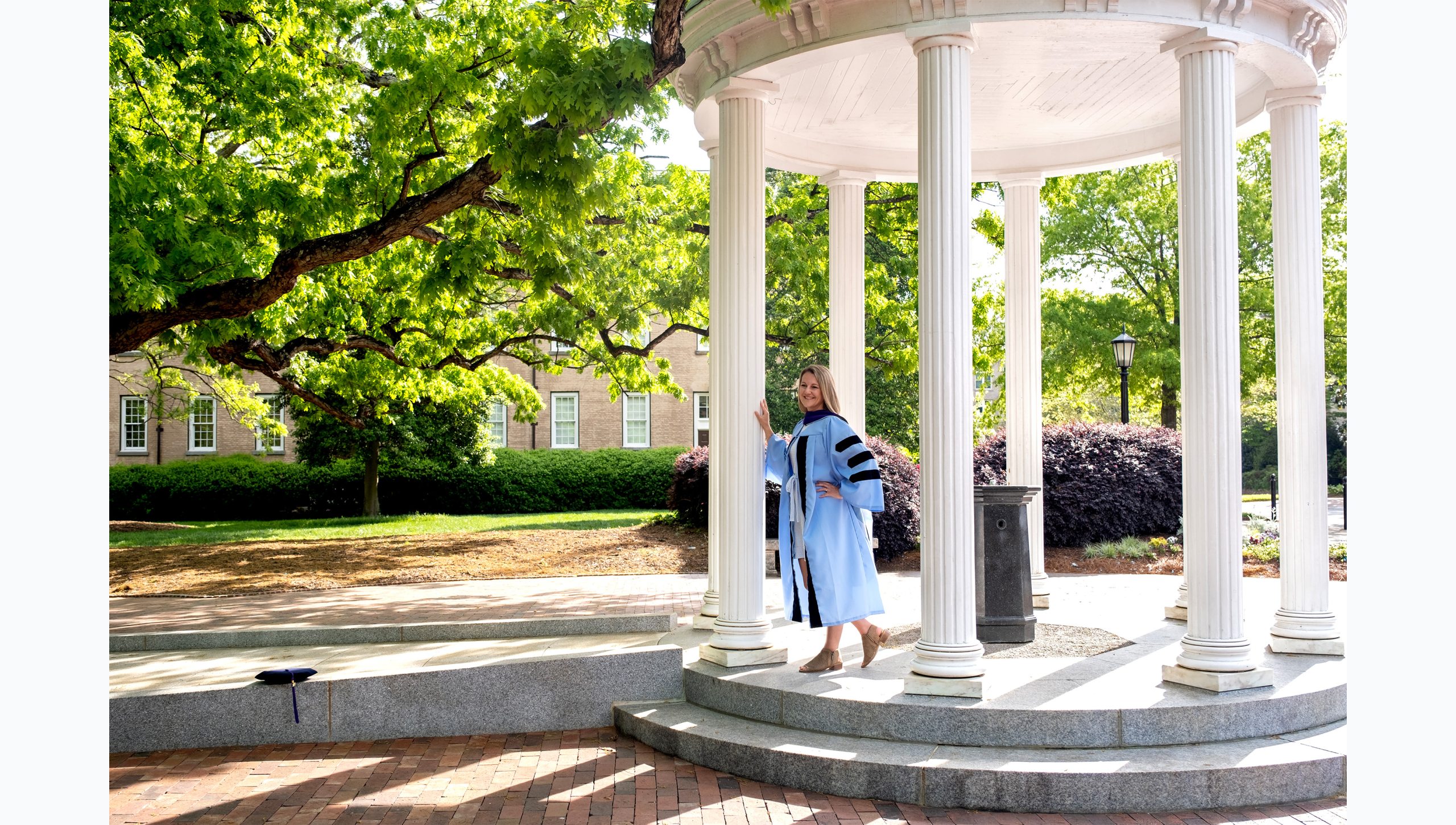 A student posing for a graduation photo at the Old Well.