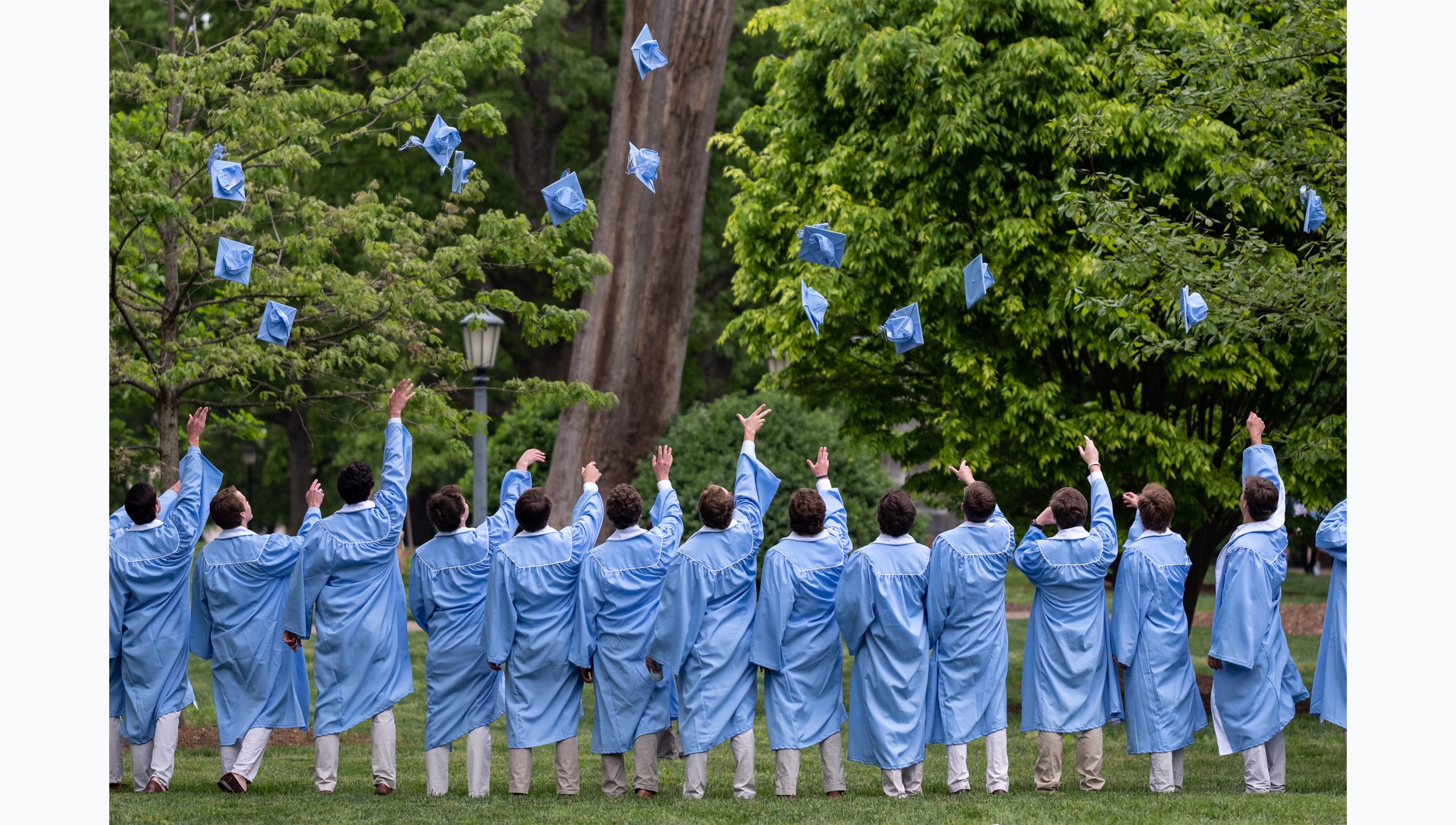 A group of students in regalia throwing caps up in their air for their group graduation photo.