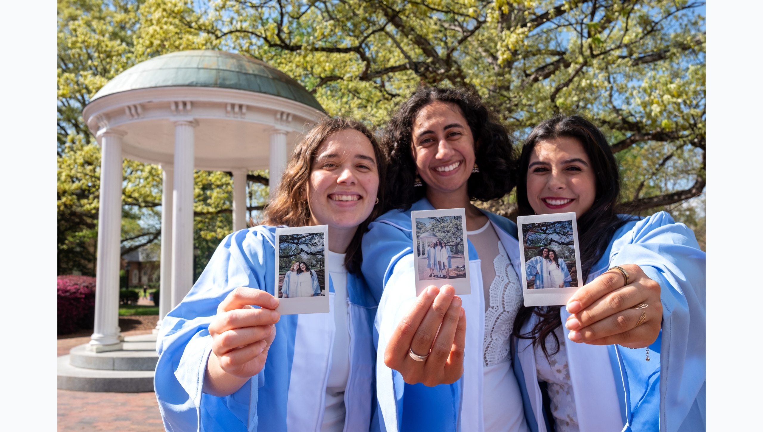 Three students holding up film photos of themselves in caps and gowns.