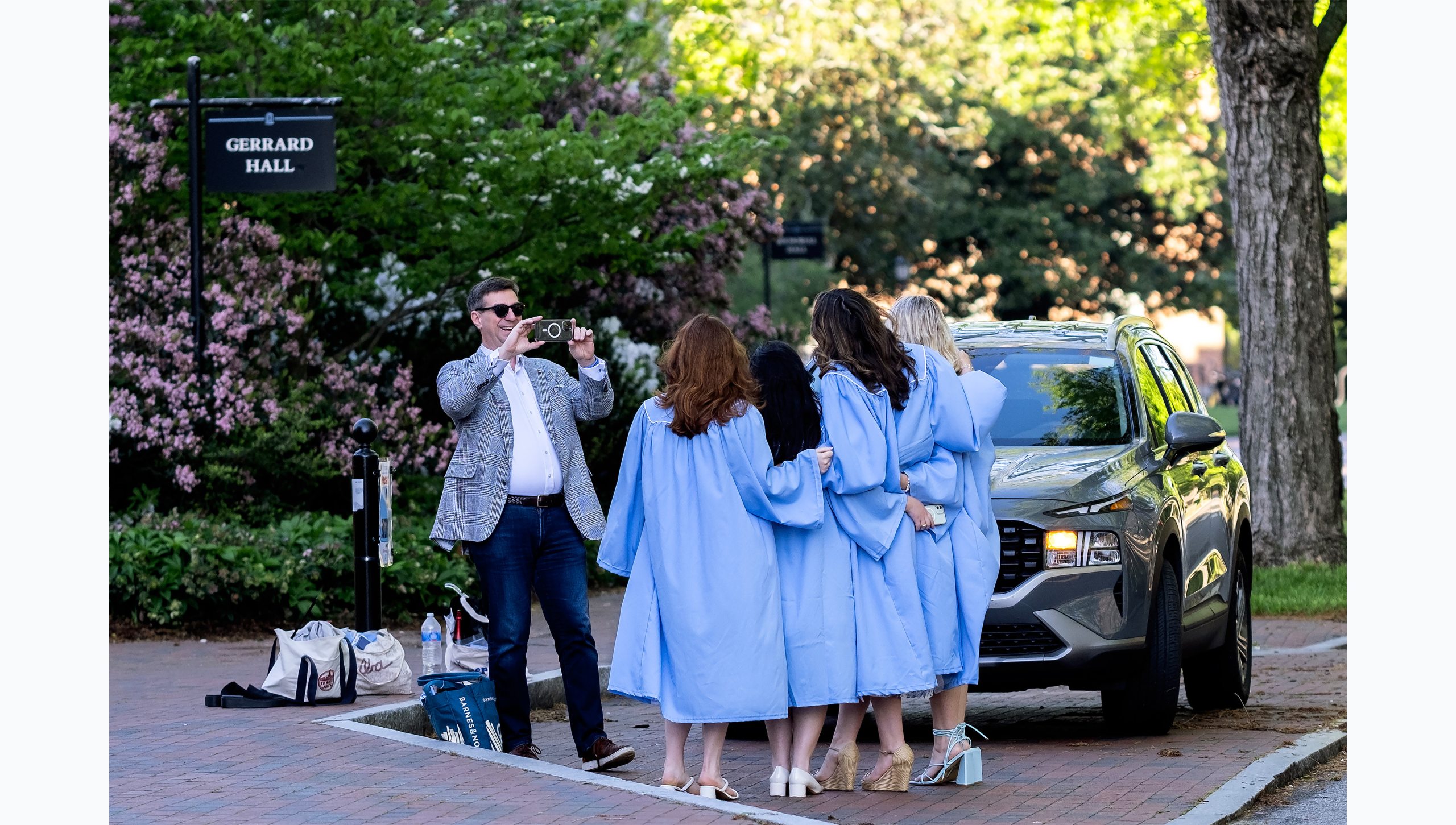A man taking a picture with a phone of a group of students in graduation gowns.