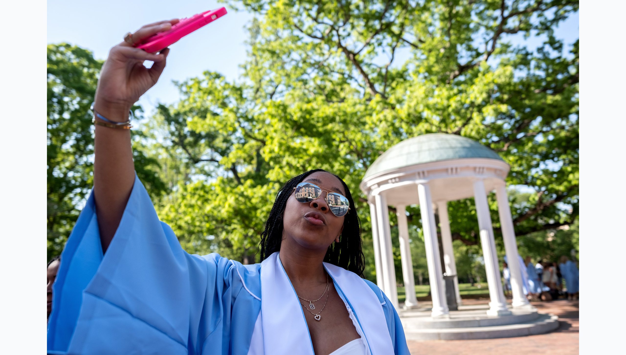 A student taking a selfie in her regalia near the Old Well.