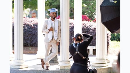 A student posing for a graduation photo at the Old Well in a suit with his graduation cap.