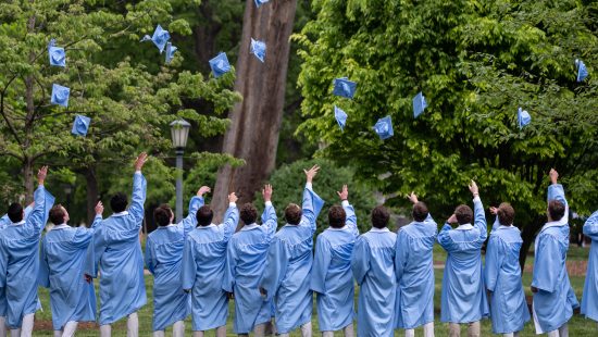 Group of students in graduation gowns throwing caps into the air