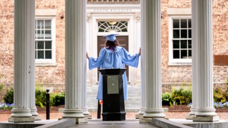Woman in graduation cap and gown standing at Old Well