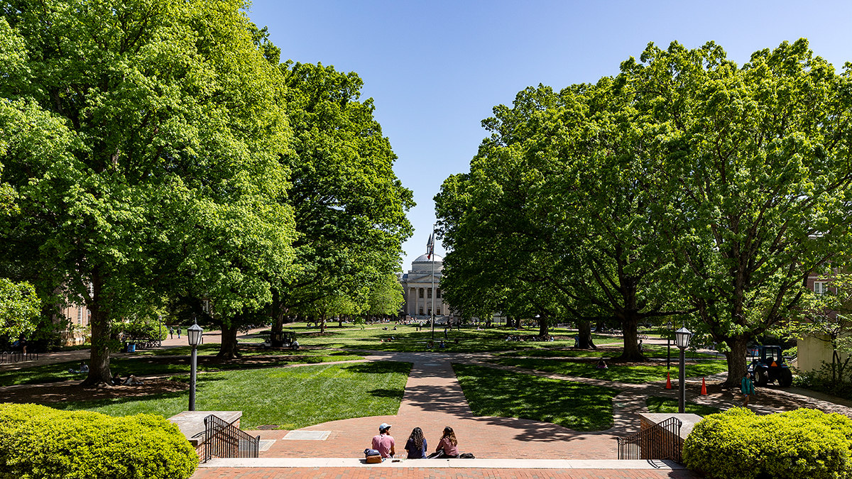 Three students sitting on the steps of South Building overlooking main campus quad.