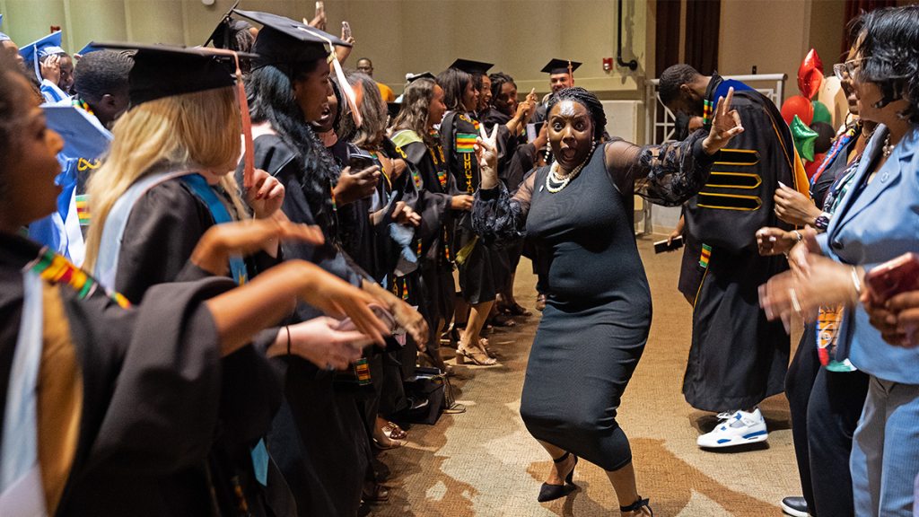 Woman dancing in front of lines of graduates